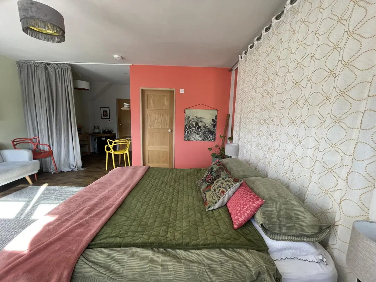 The bed against the coral wall, with the kitchen corner beyond